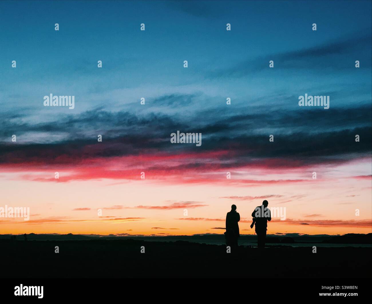 People walking along Dunbar beach silhouetted by the sunset - Smartphone Captured Stock Image