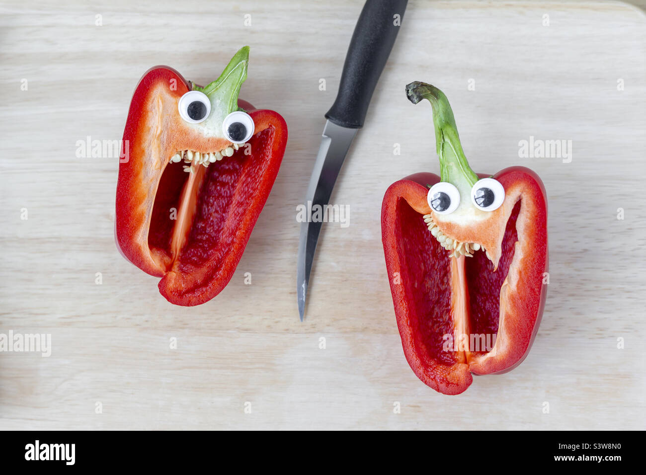 Sweet pepper cut in half with knife in the middle of the frame, googly eyes Stock Photo