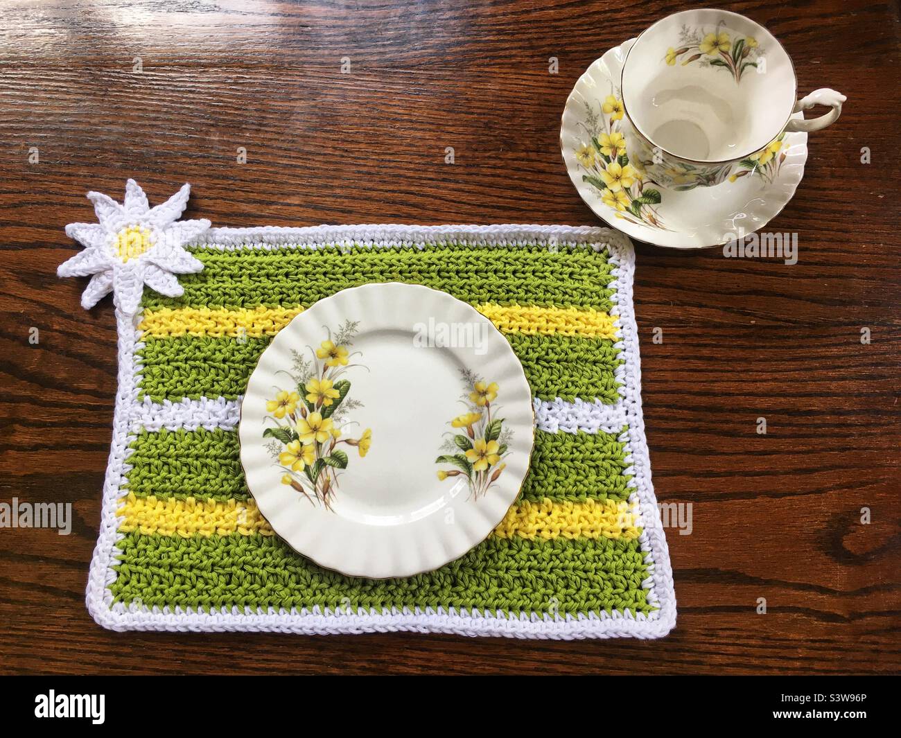 Yellow, green and white Richmond bone china with a flower pattern on a table with a matching handmade crochet placemat Stock Photo