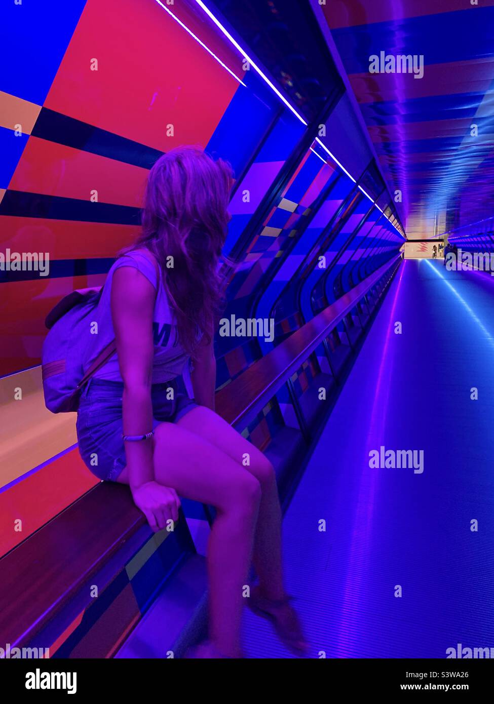 Girl sitting in a colourful tunnel looking towards the exit light Stock Photo