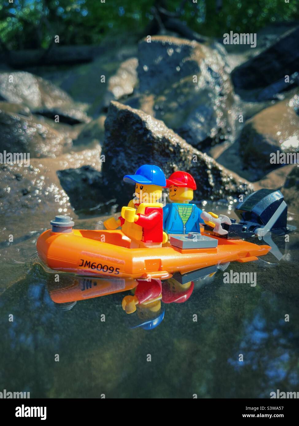 Lego figures in a red Rubber dinghy with outboard engine on muddy Water Stock Photo
