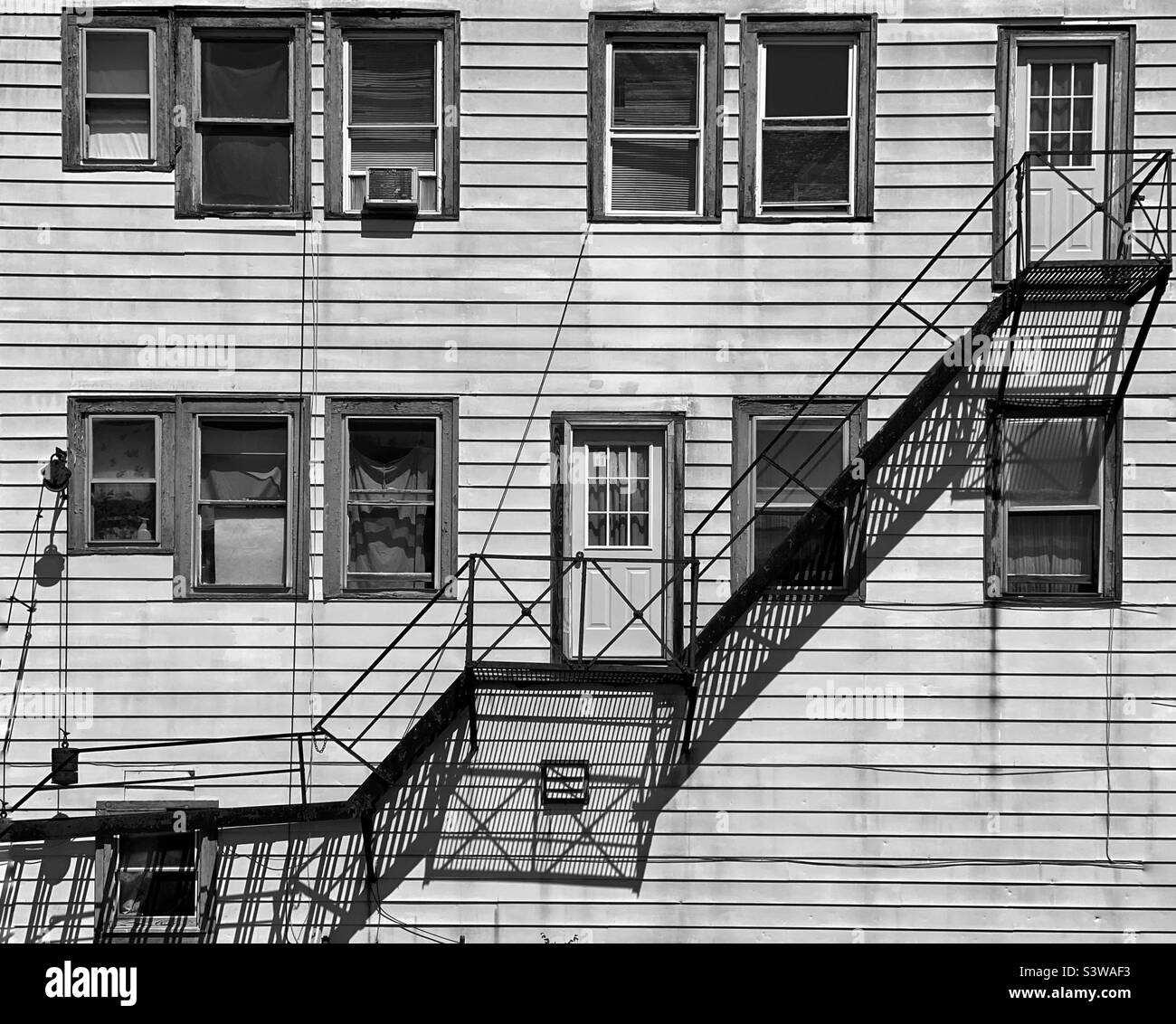 Fire escape and its shadow on the side of a wooden building Stock Photo