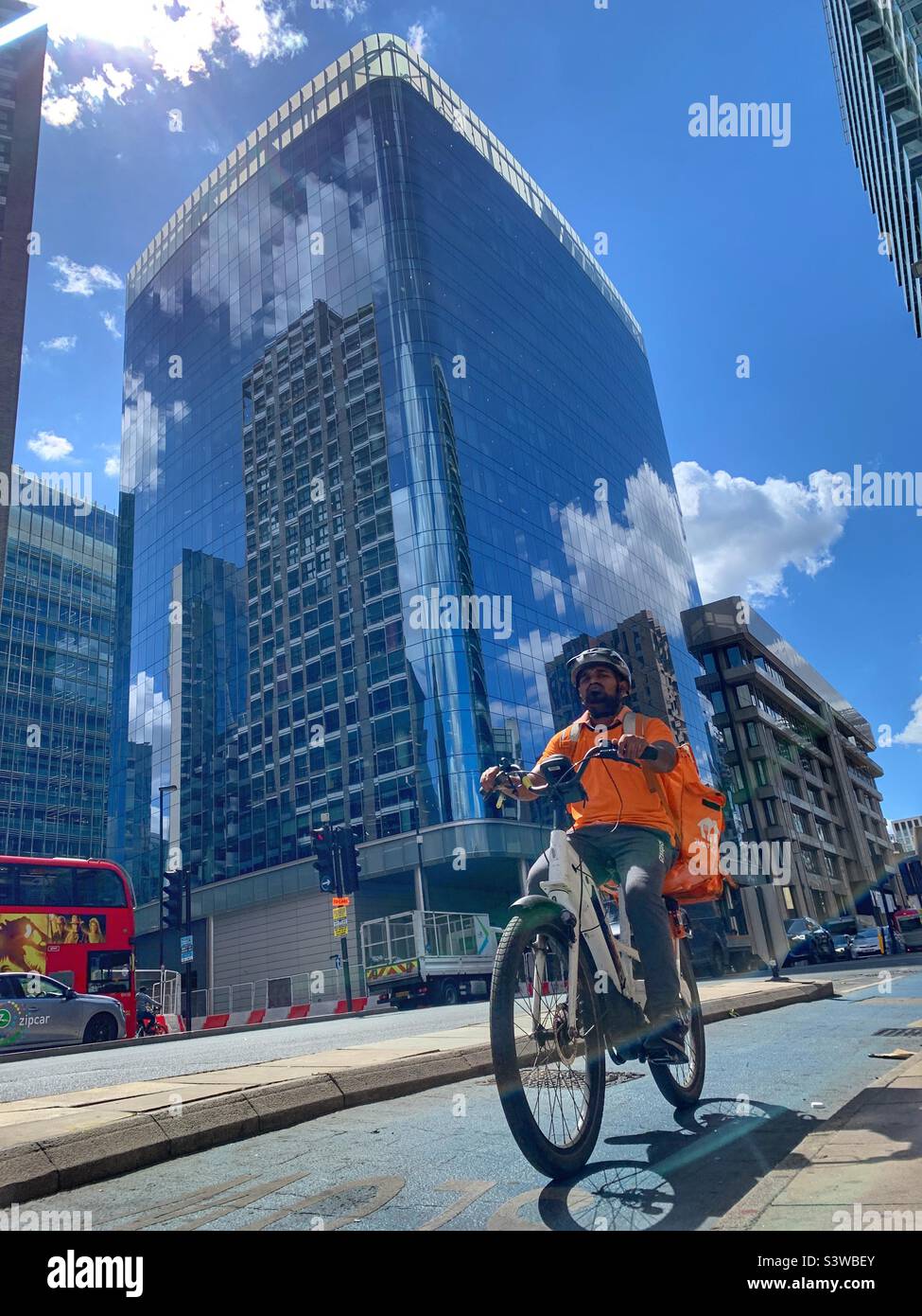 Just eat Delivery cyclist in orange on London’s Whitechapel road in summer - Smartphone Captured Stock Image