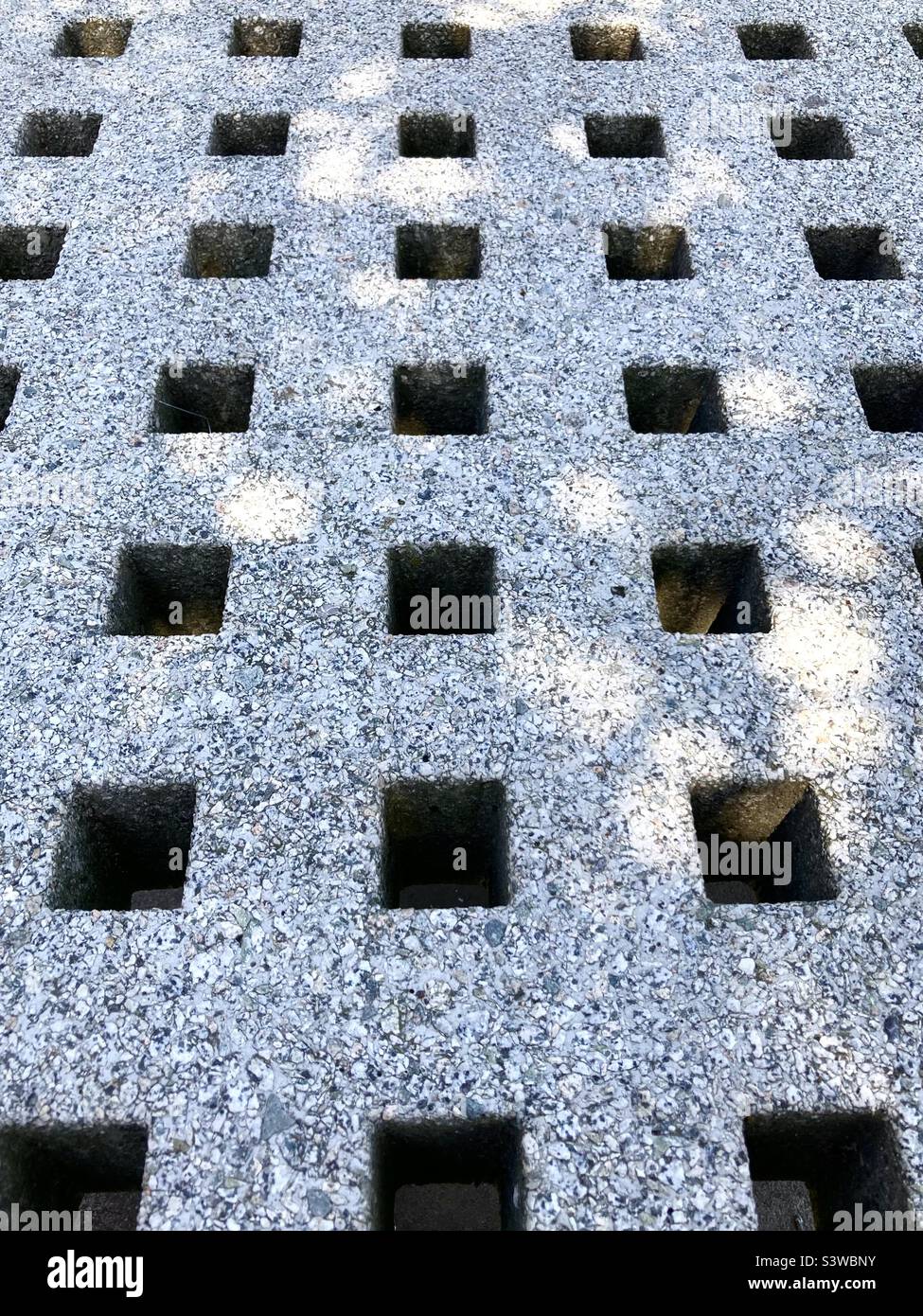 Concrete bench with square holes in dappled sunlight close up - Smartphone Captured Stock Image