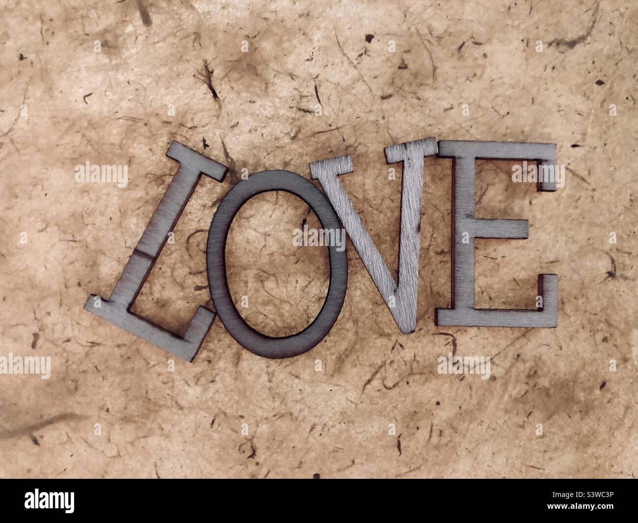 “LOVE” typography wooden letters handmade paper texture background. Stock Photo