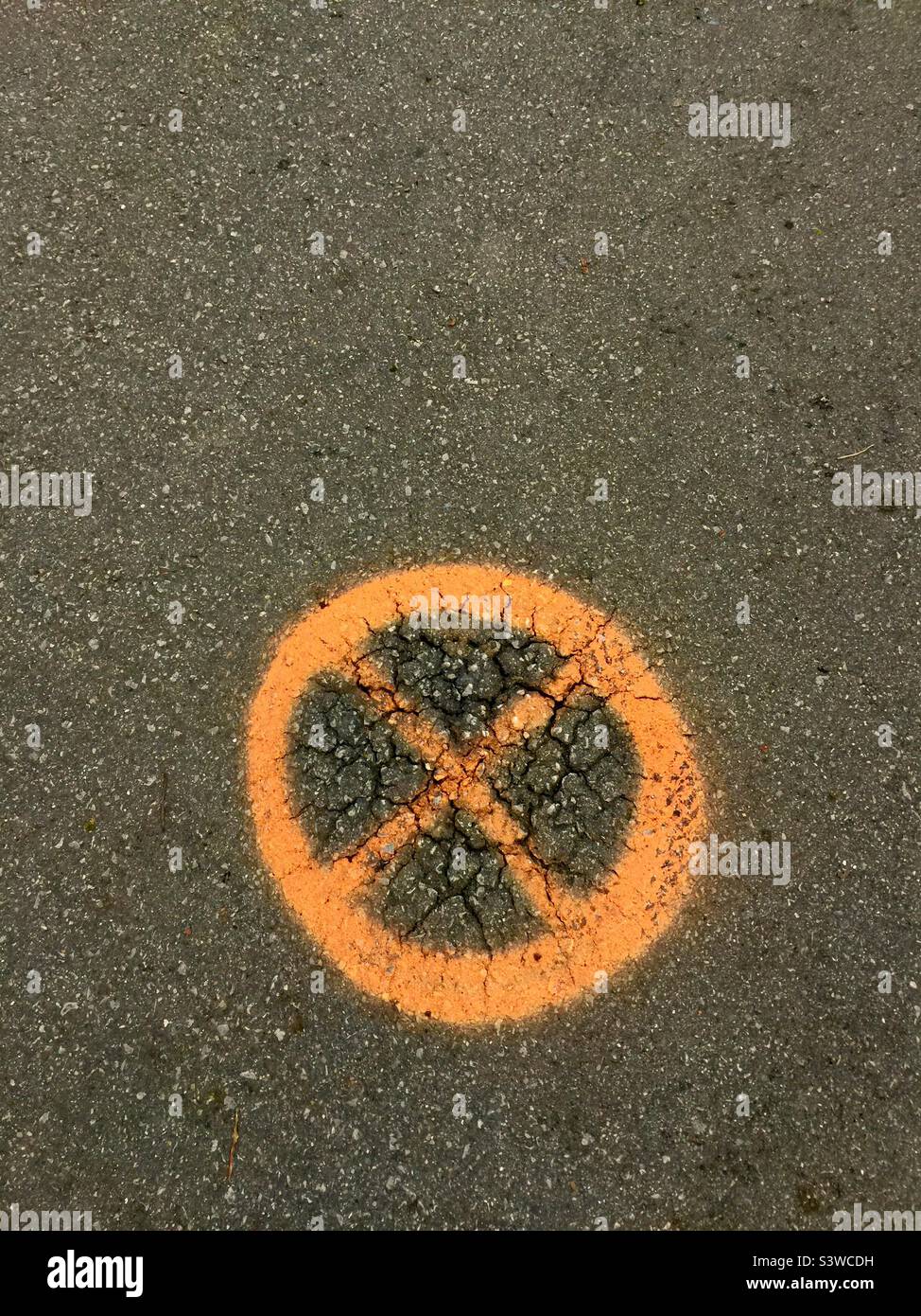 An orange coloured circle and cross on the road, Ontario, Canada. Symbol. Icon. X in a circular shape. Four. Quadrants. Quarters. Equal pieces of a pie. - Smartphone Captured Stock Image