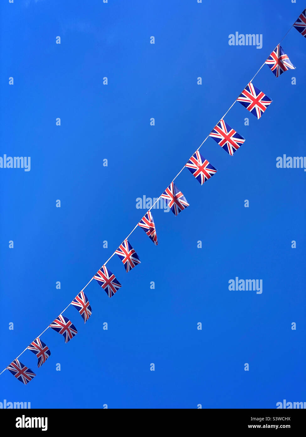 Union Jack bunting, flapping in a blue British summer sky. Photo ©️ COLIN HOSKINS. Stock Photo