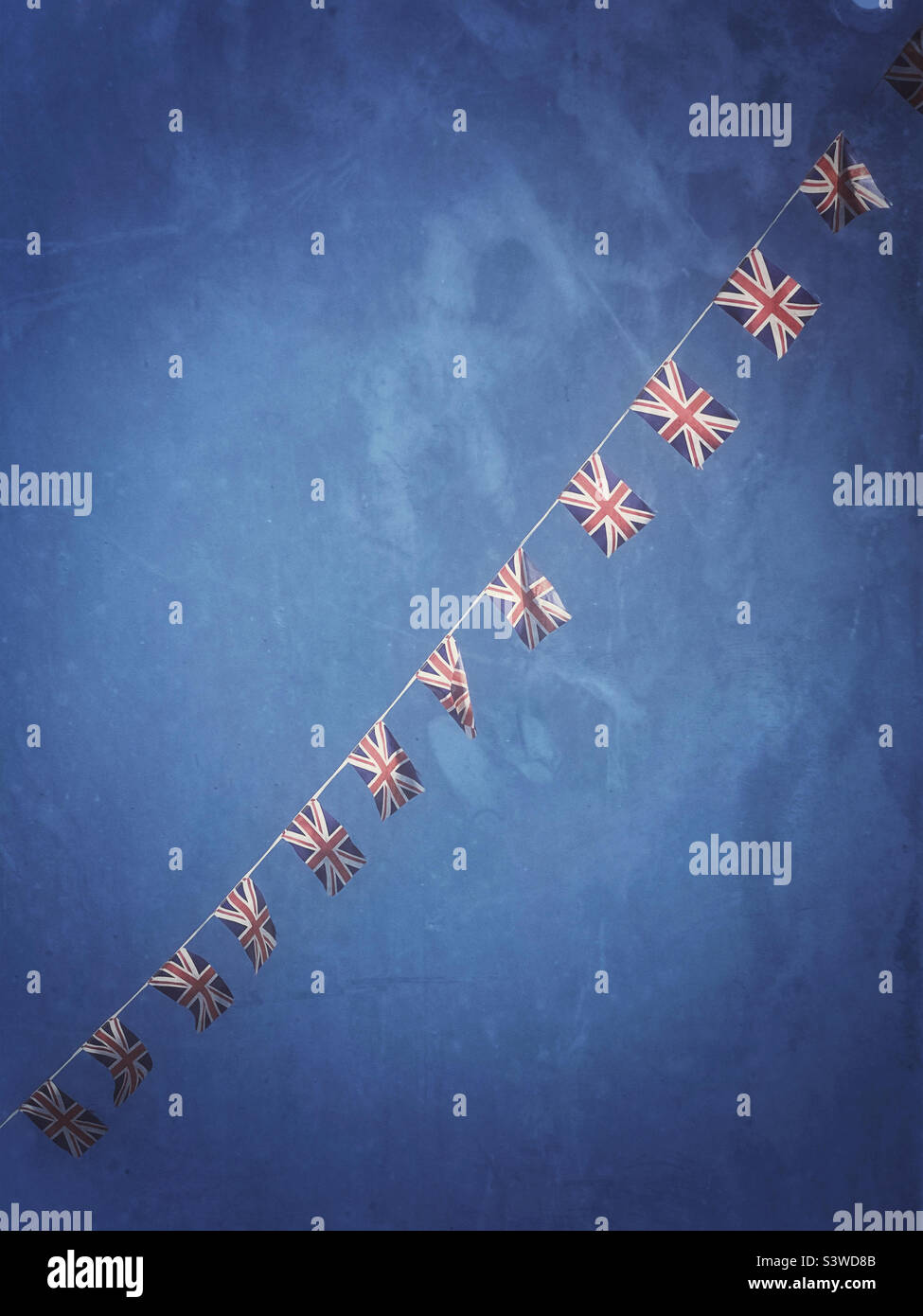 Desaturated and faded Union Jack flags fly in a murky sky on a string of bunting. Is this a visual comment on the effects of Brexit - the UK no longer as dynamic as before? Photo ©️ COLIN HOSKINS. Stock Photo