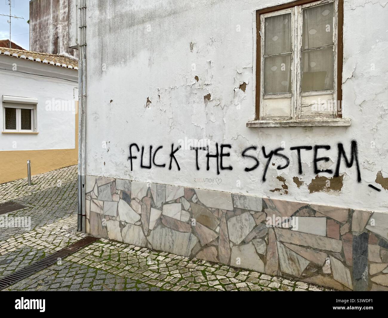 ‘Fuck the System’ written on the side wall of a building on a residential street in Lagos, Portugal Stock Photo