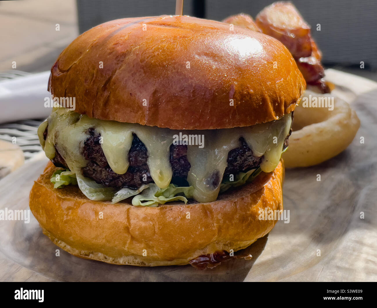 Cheeseburger with melted cheese and onion rings on a wooden platter - Smartphone Captured Stock Image
