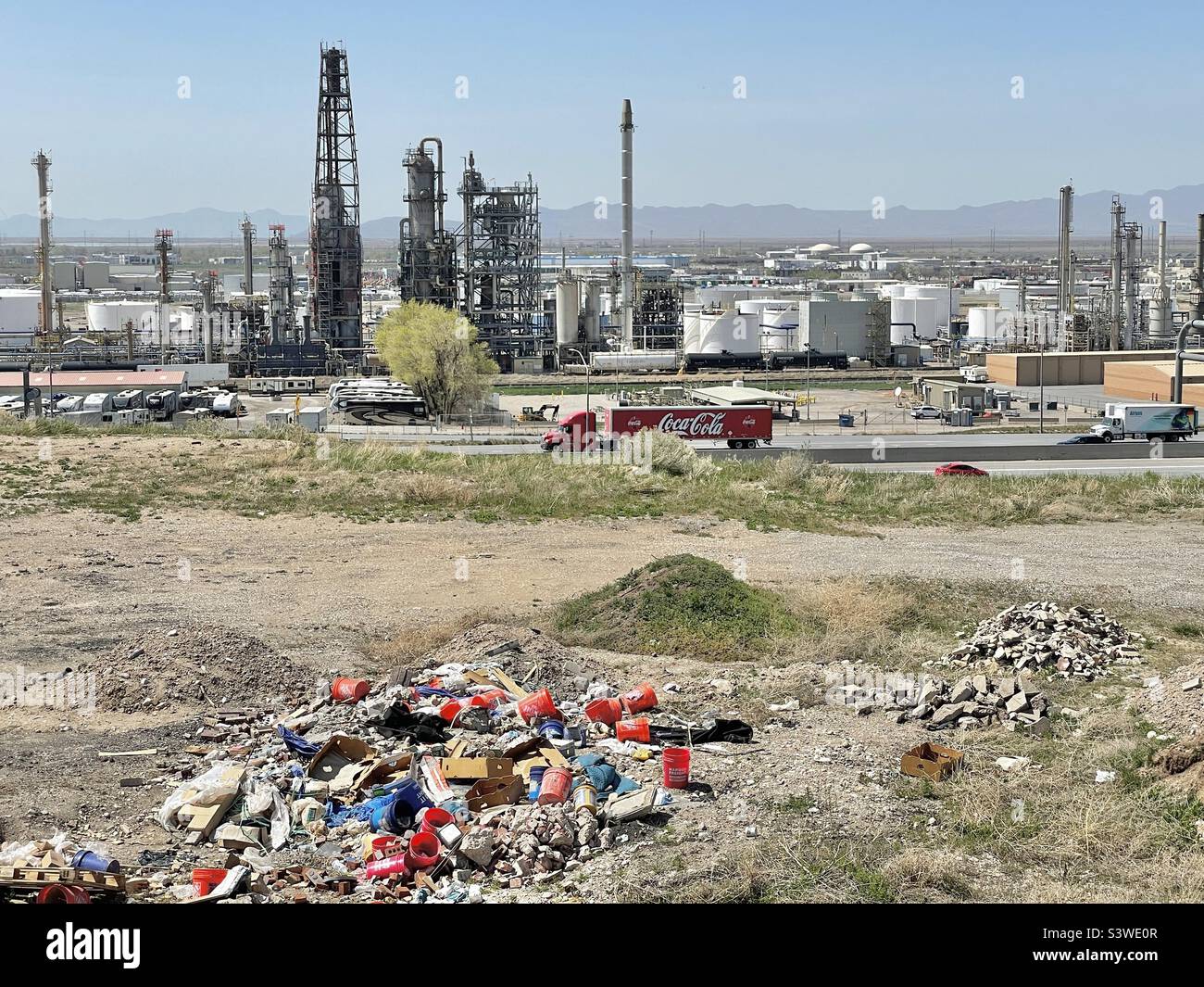 An open field in an Utah, USA industrial area; Oil refinery can be seen in the background. Garbage and trash can be seen that workemen have dumped. - Smartphone Captured Stock Image