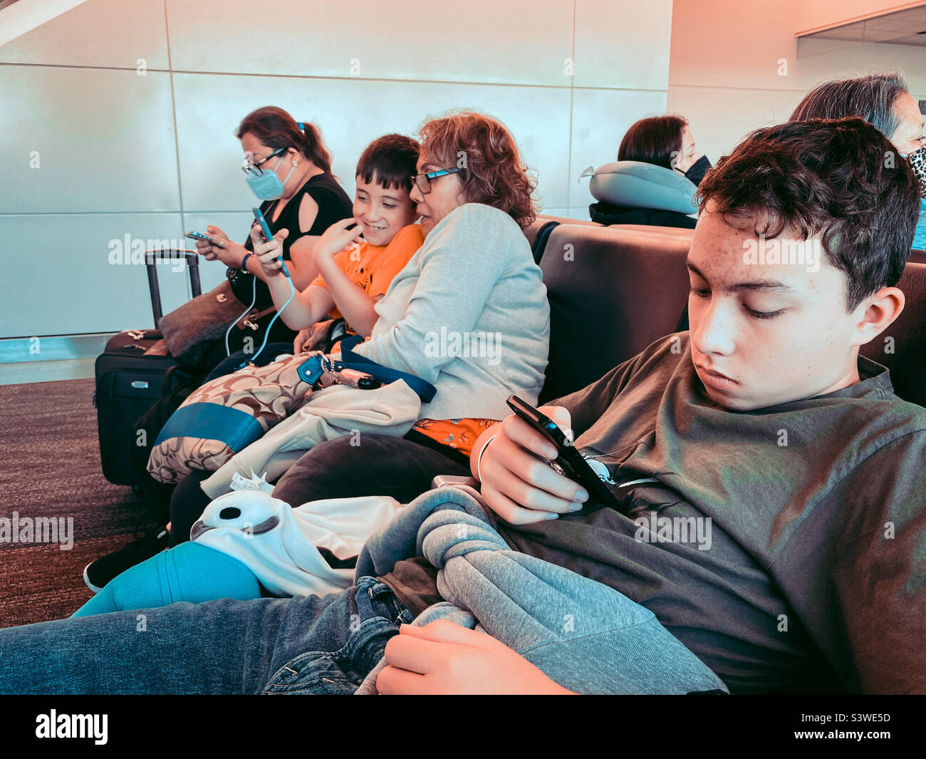 A family sit together on seats at the departure gate at San Francisco International Airport while waiting to board a flight. - Smartphone Captured Stock Image