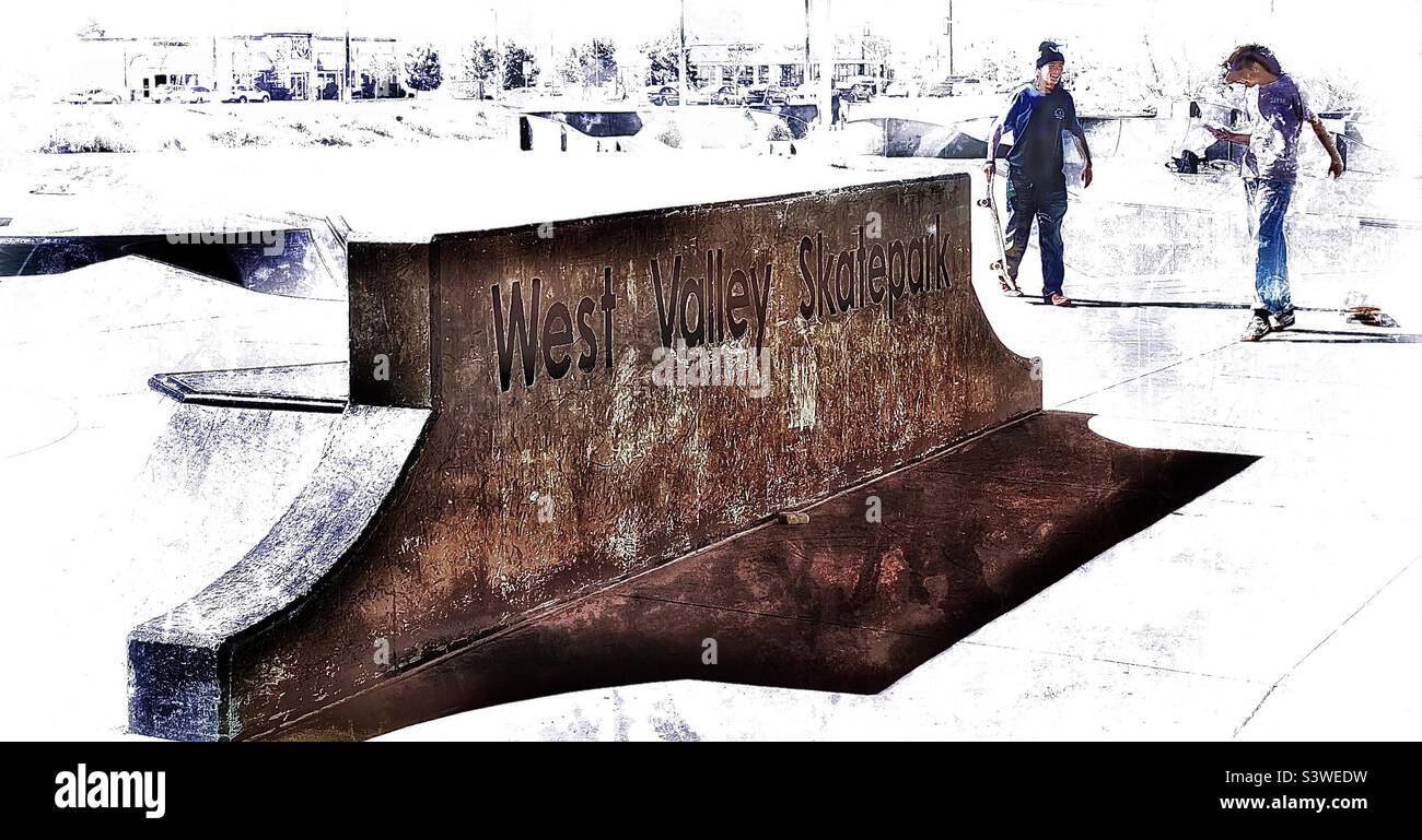A dramatic, high-key image of a local skatepark in Utah, USA. Two skateboarders stand out in the background, while the large, shadowed stone signage leads the eye to them. - Smartphone Captured Stock Image