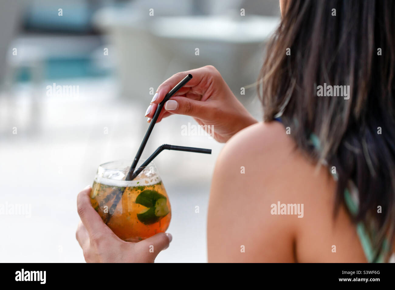 Young woman drinking delicious cocktail by the pool, happy hour Stock Photo