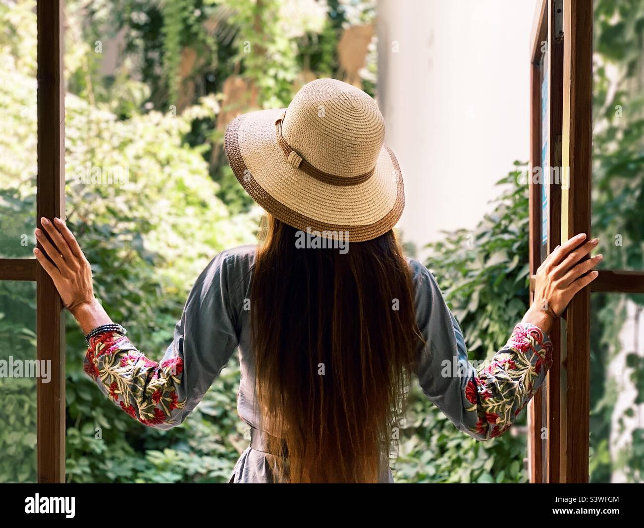 Young woman with long hair standing at the opened window - Smartphone Captured Stock Image