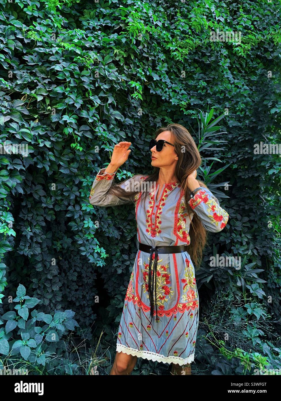 Young woman with long hair surrounded by green tropical plants - Smartphone Captured Stock Image
