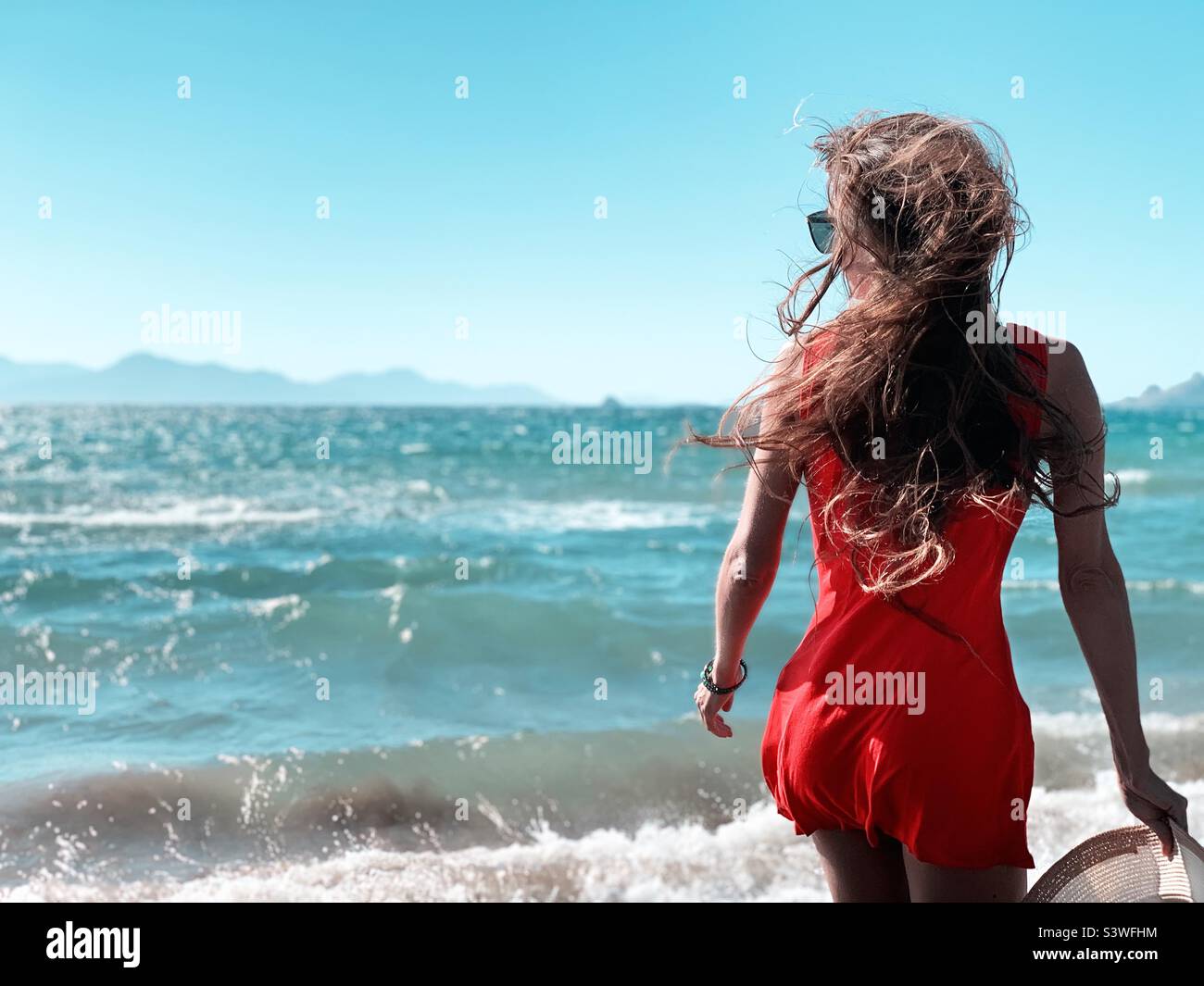 Young woman walking by the seaside in red summer dress - Smartphone Captured Stock Image