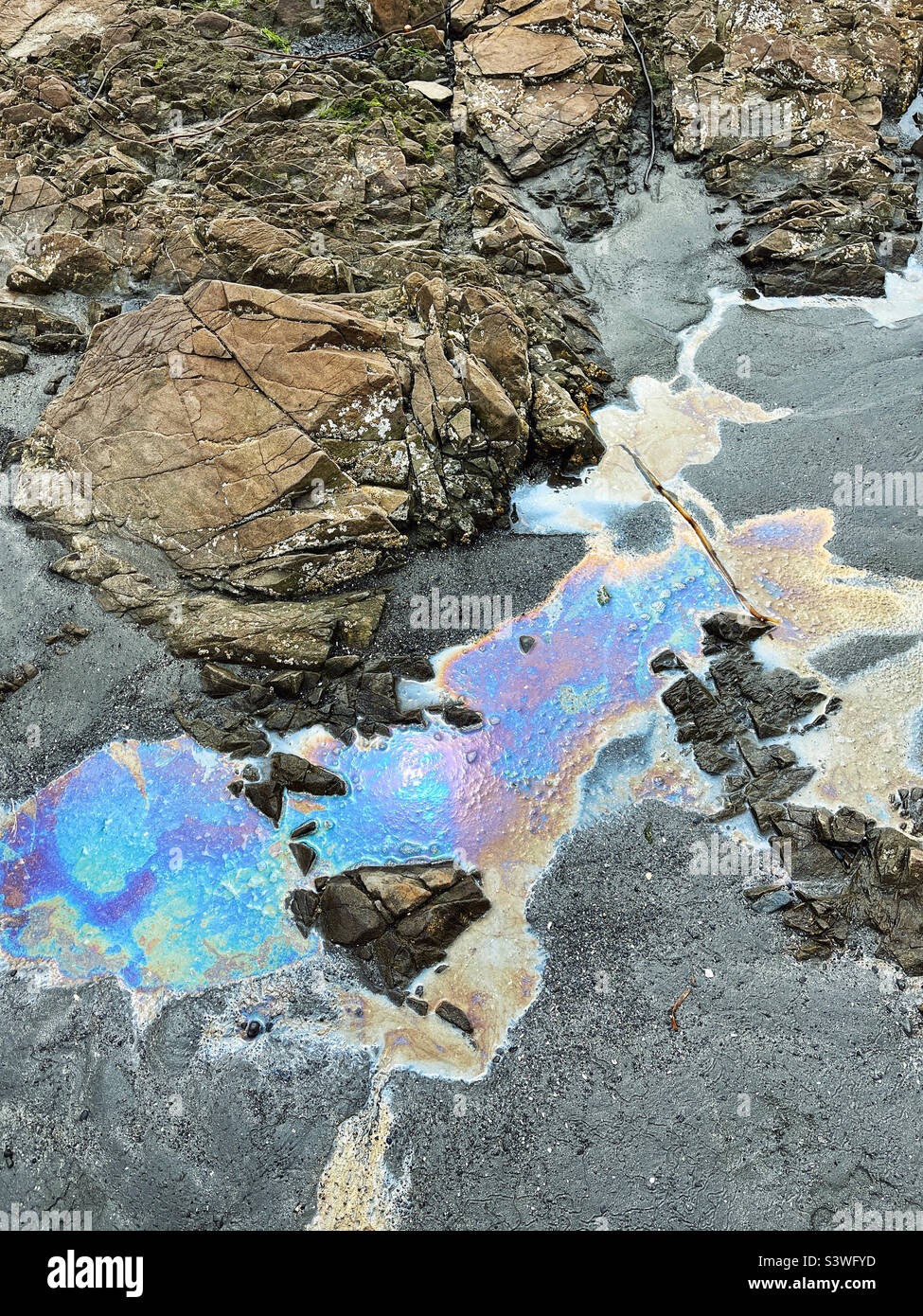 Oil spill creates rainbow pools on a Pacific Ocean Beach Stock Photo