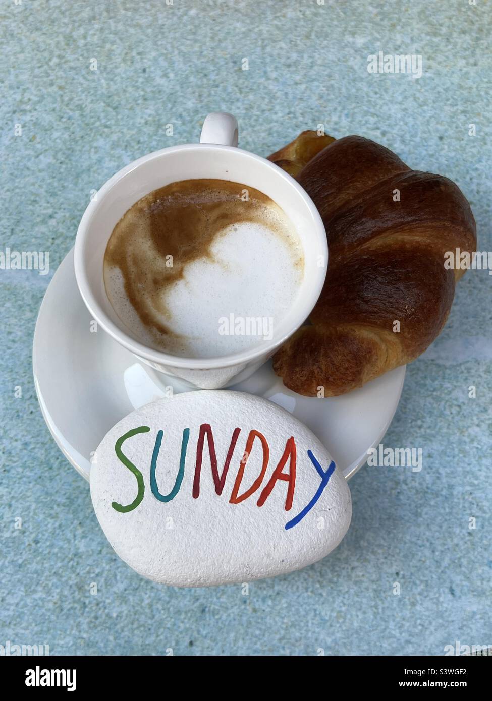 Sunday breakfast with a creative colored stone, cappuccino and croissant - Smartphone Captured Stock Image