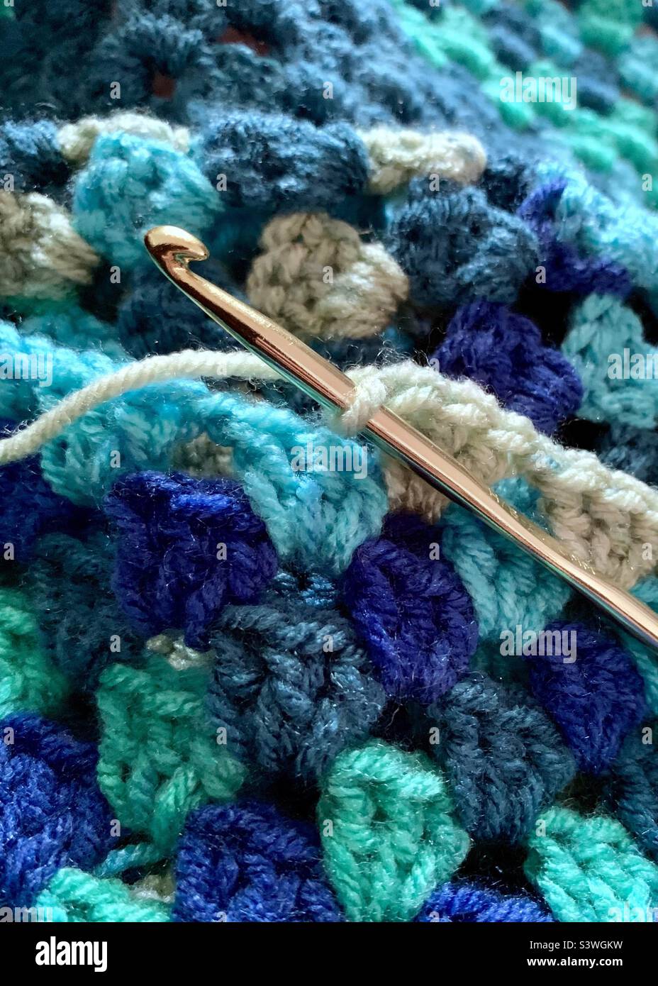 Gold aluminum crochet hook with granny square blanket in shades of blue