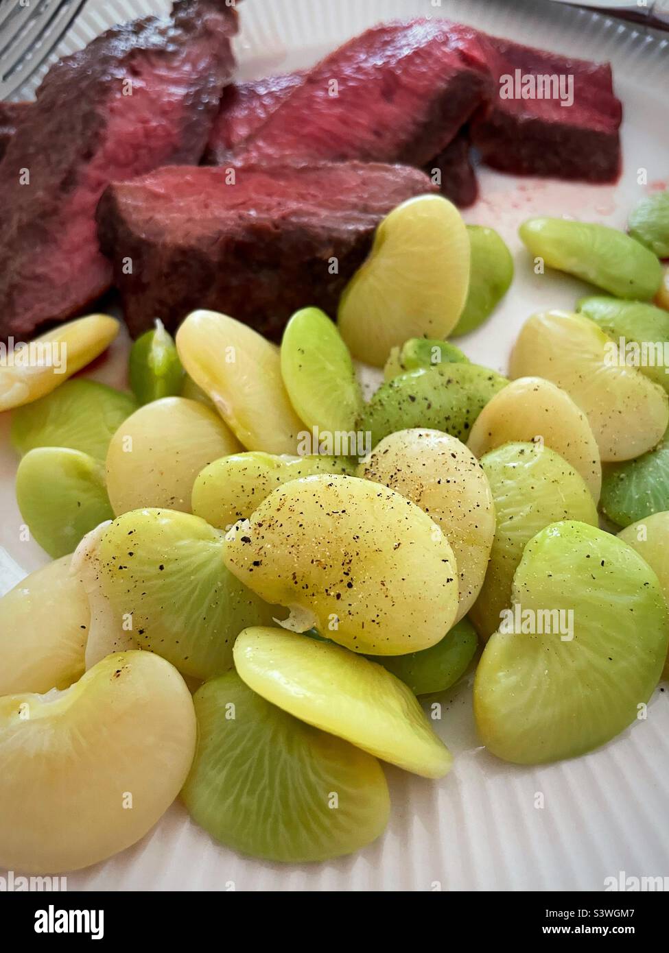 Close up of a meal of medium rare flank steak and freshly steamed lima beans, 2022, USA - Smartphone Captured Stock Image