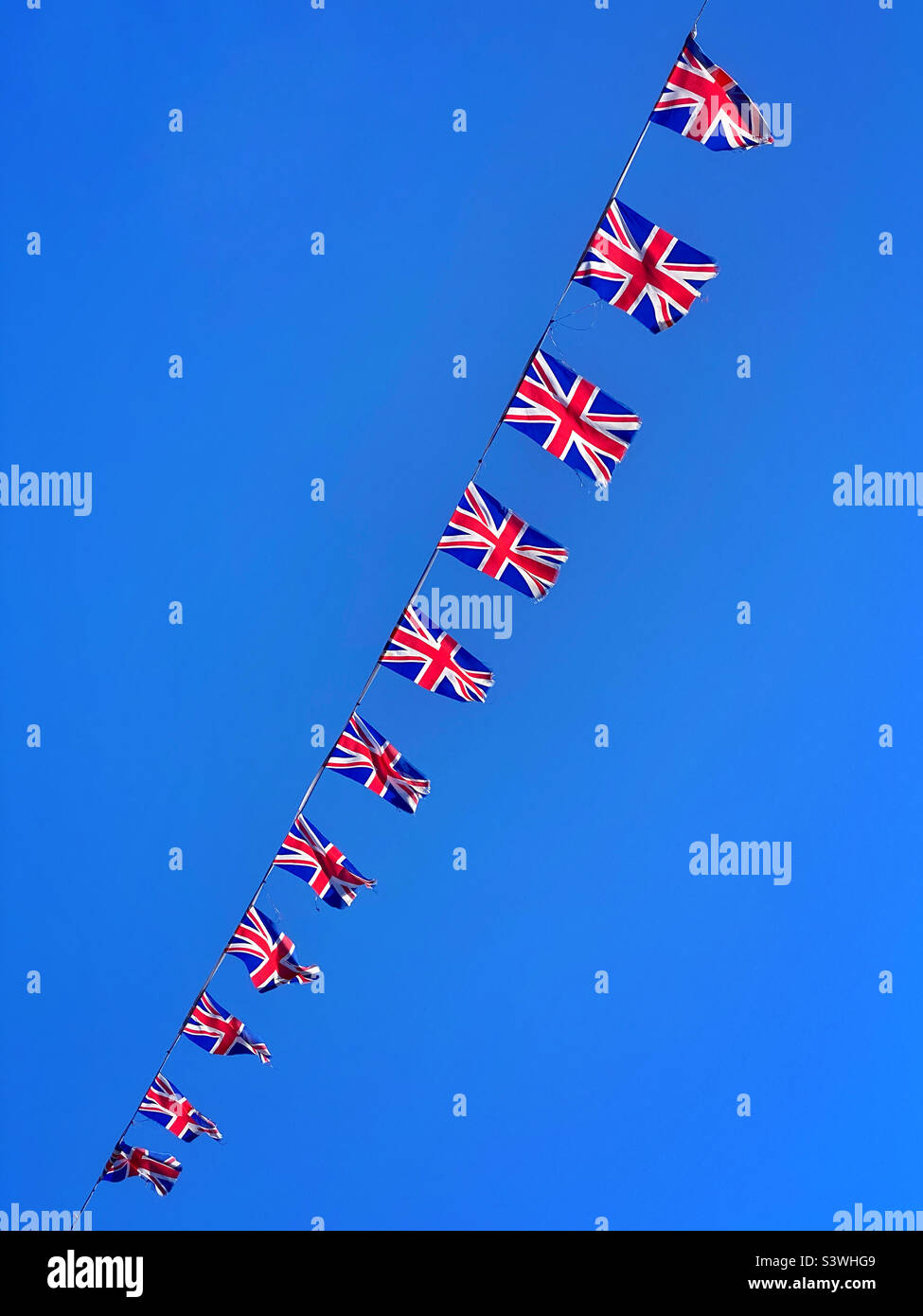 Union Jack flags flying in the sunny blue sky of a British summer. It’s the Queen’s Platinum Jubilee celebrations-a unique & historic event is celebrated. Britain at it’s best? Photo ©️ COLIN HOSKINS. Stock Photo