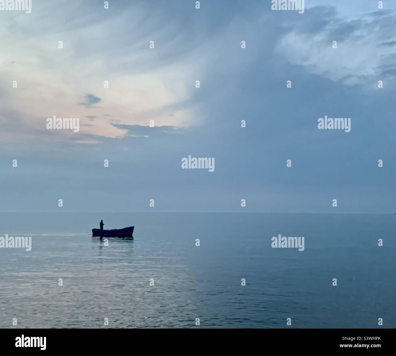 Boat and fisherman on calm misty sea - Smartphone Captured Stock Image