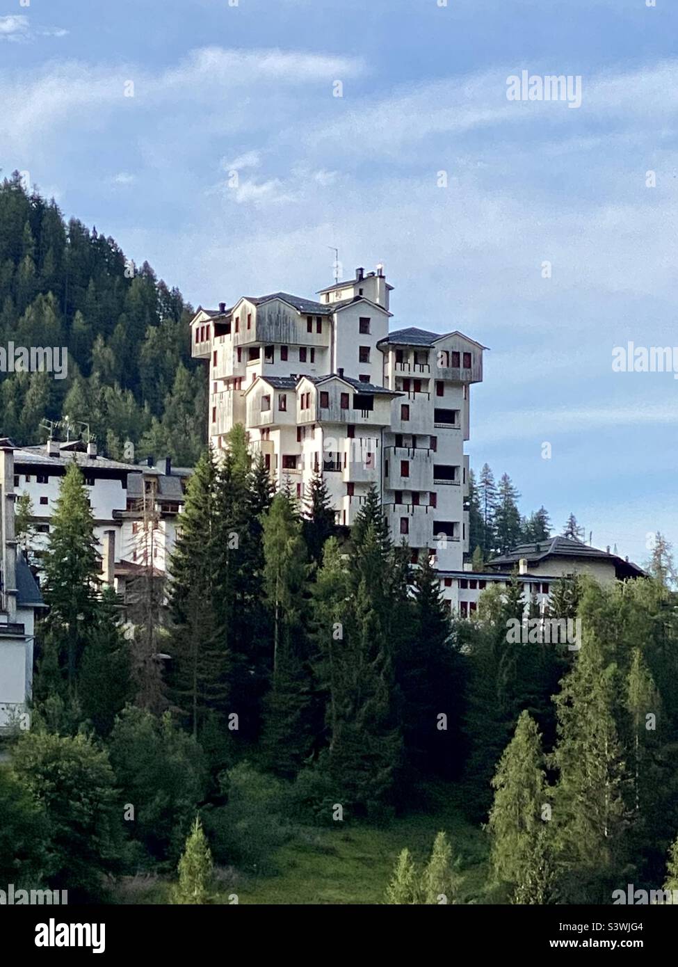 Scenic Alpine Village With Tall Unusual White Hotel Amid Dense Pine Forest - Smartphone Captured Stock Image