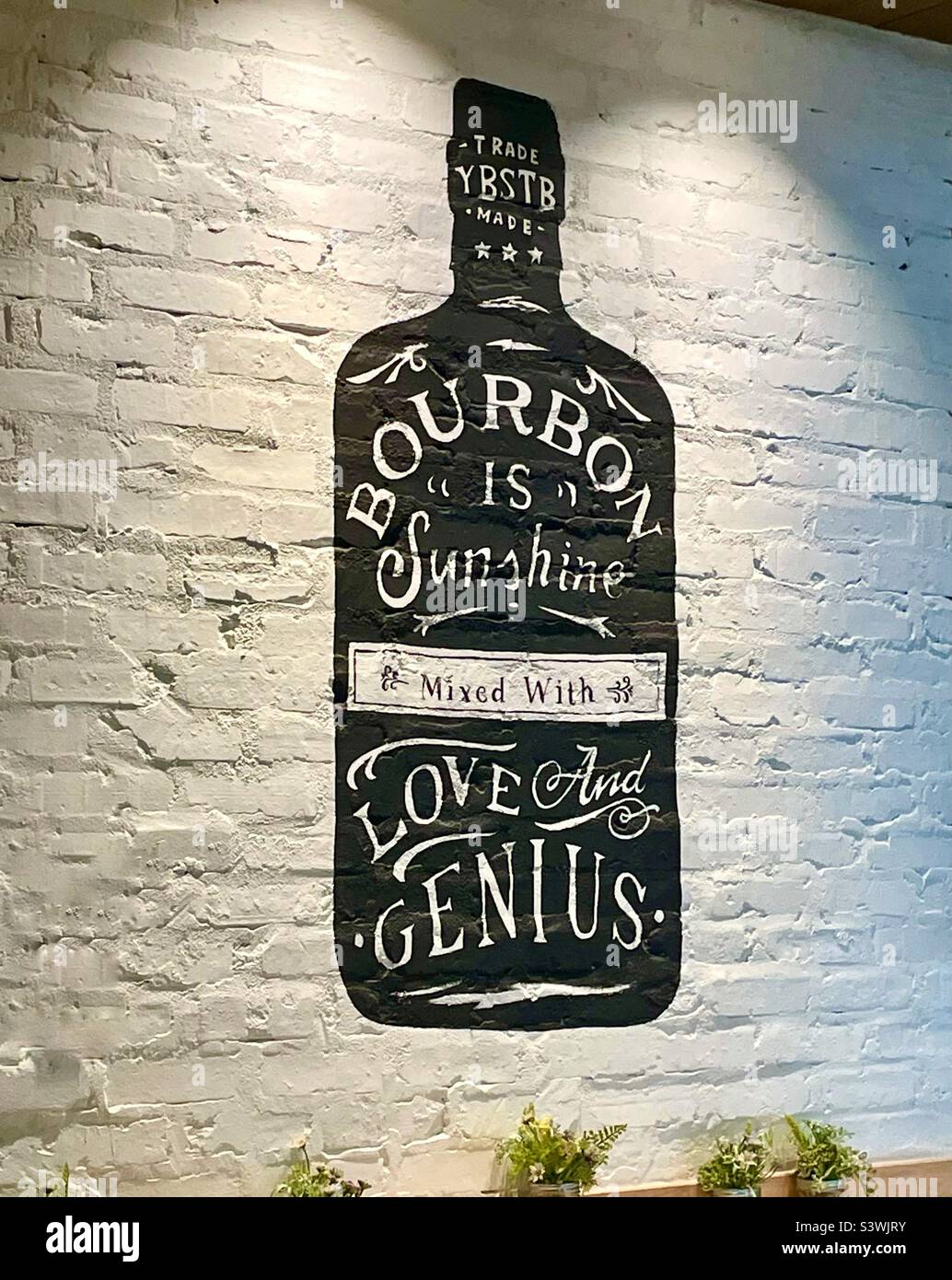 Funny hand painted sign on a white brick wall in a bar in. Miami airport Shang bourbon is sunshine mixed with love and genius - Smartphone Captured Stock Image