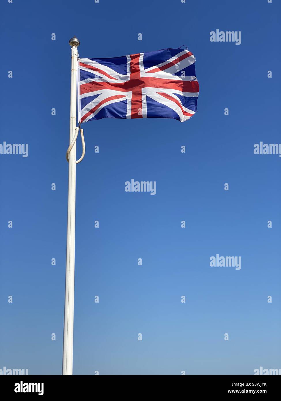 The Union Jack - flag of The United Kingdom, Great Britain & Northern Ireland, flutters in a sunny blue sky. This flag can be seen in England, Scotland, Wales & N.I. Photo ©️ COLIN HOSKINS. Stock Photo