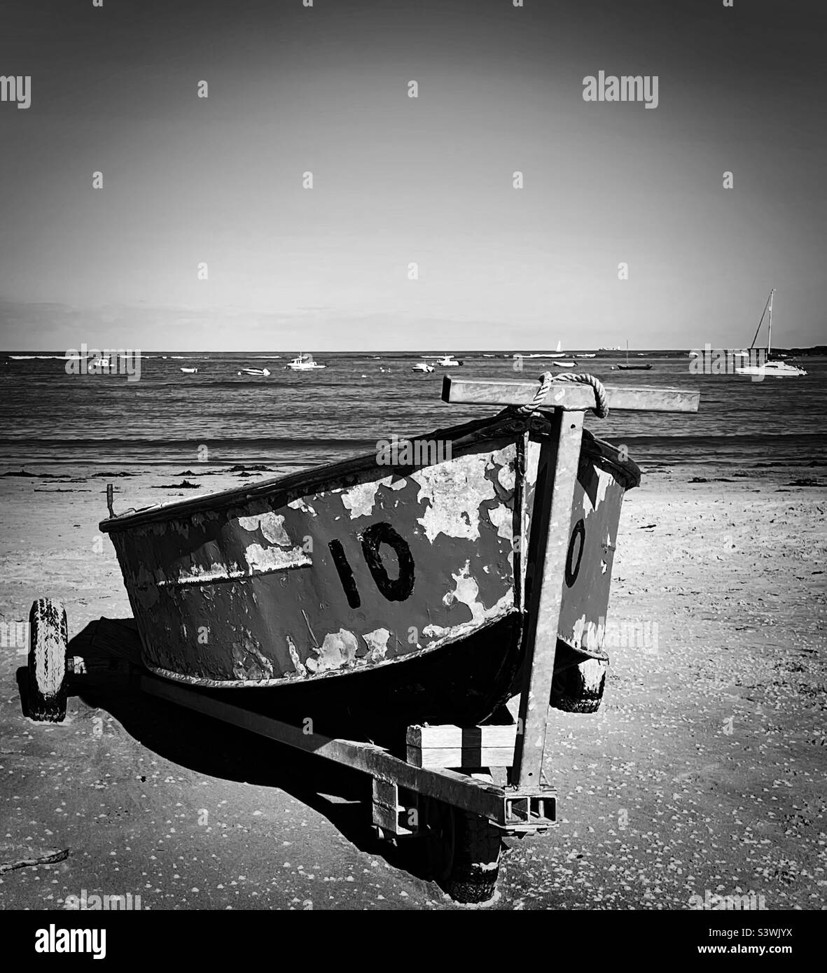 ‘Number 10’ an old boat sits on the shore, envious of the newer, younger models on the water (Black & White) Stock Photo