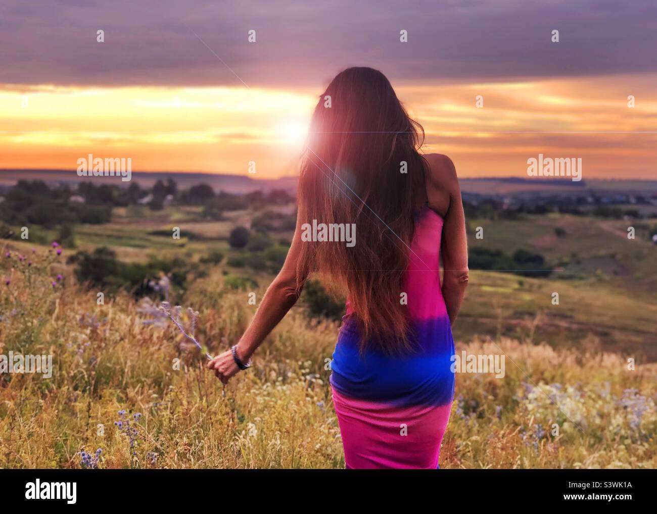 Young woman with long hair enjoying beautiful sunset over the field - Smartphone Captured Stock Image