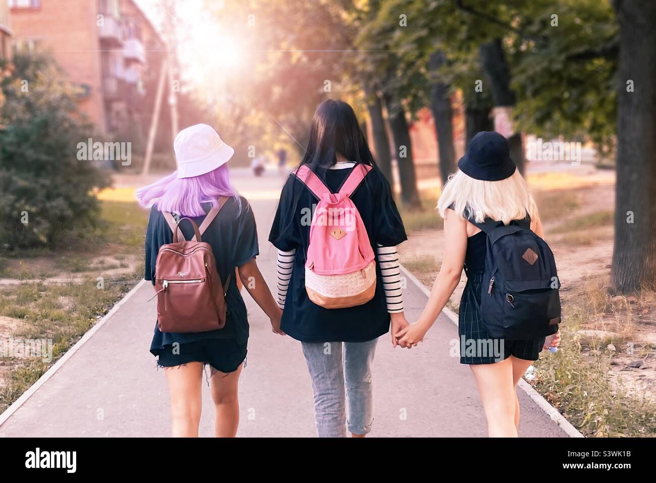 Three teenagers students walking together with backpacks by the city street Stock Photo