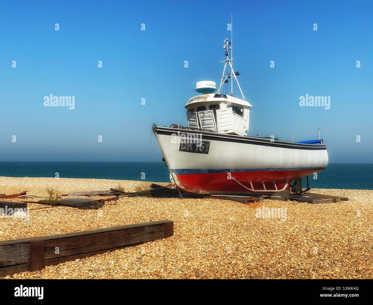 A lone fishing trawler boat has been brought ashore and now lies dormant on a pebble beach. Photo ©️ COLIN HOSKINS. Stock Photo