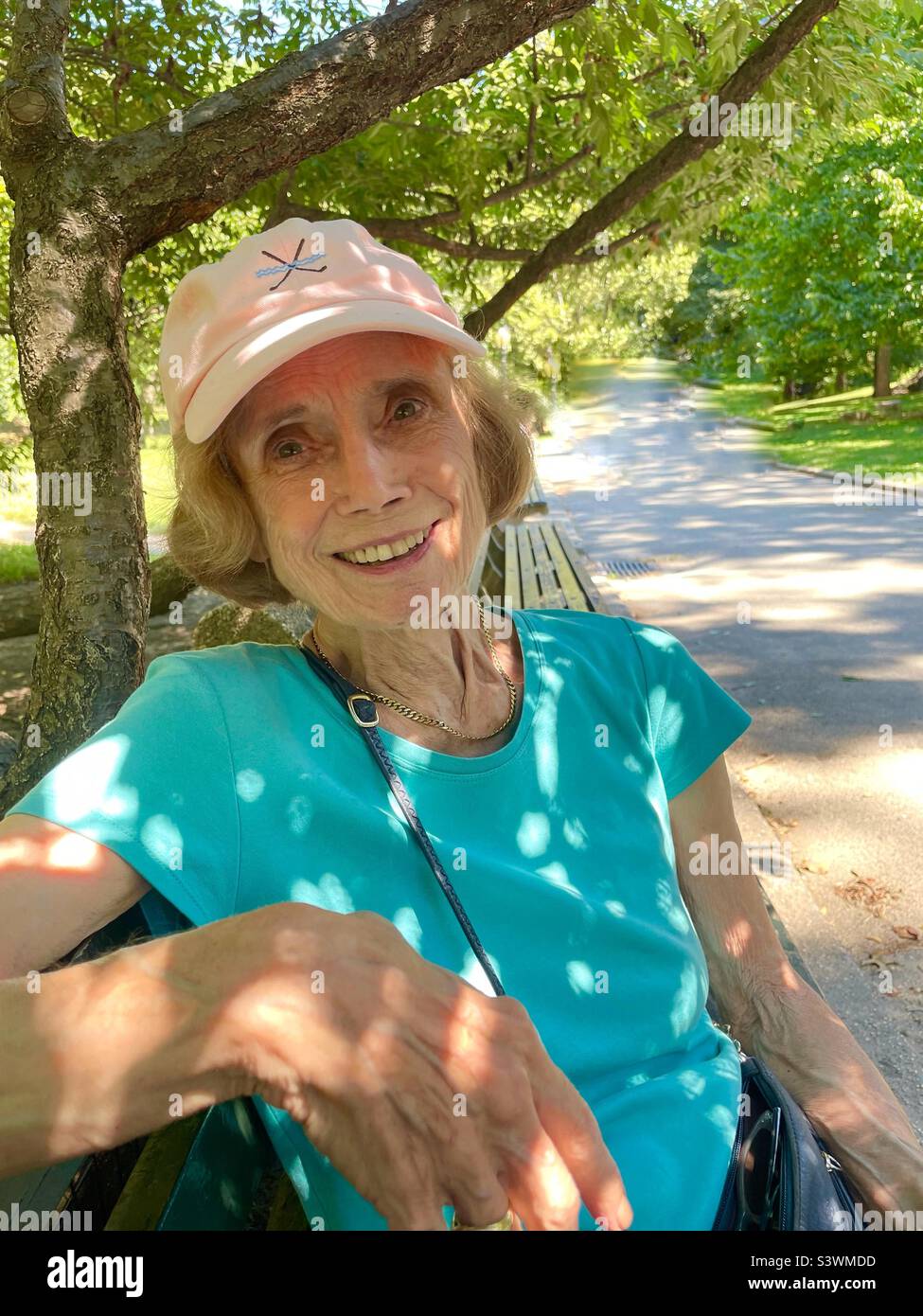 A smiling senior woman sits under the trees in Central Park, New York City, USA - Smartphone Captured Stock Image