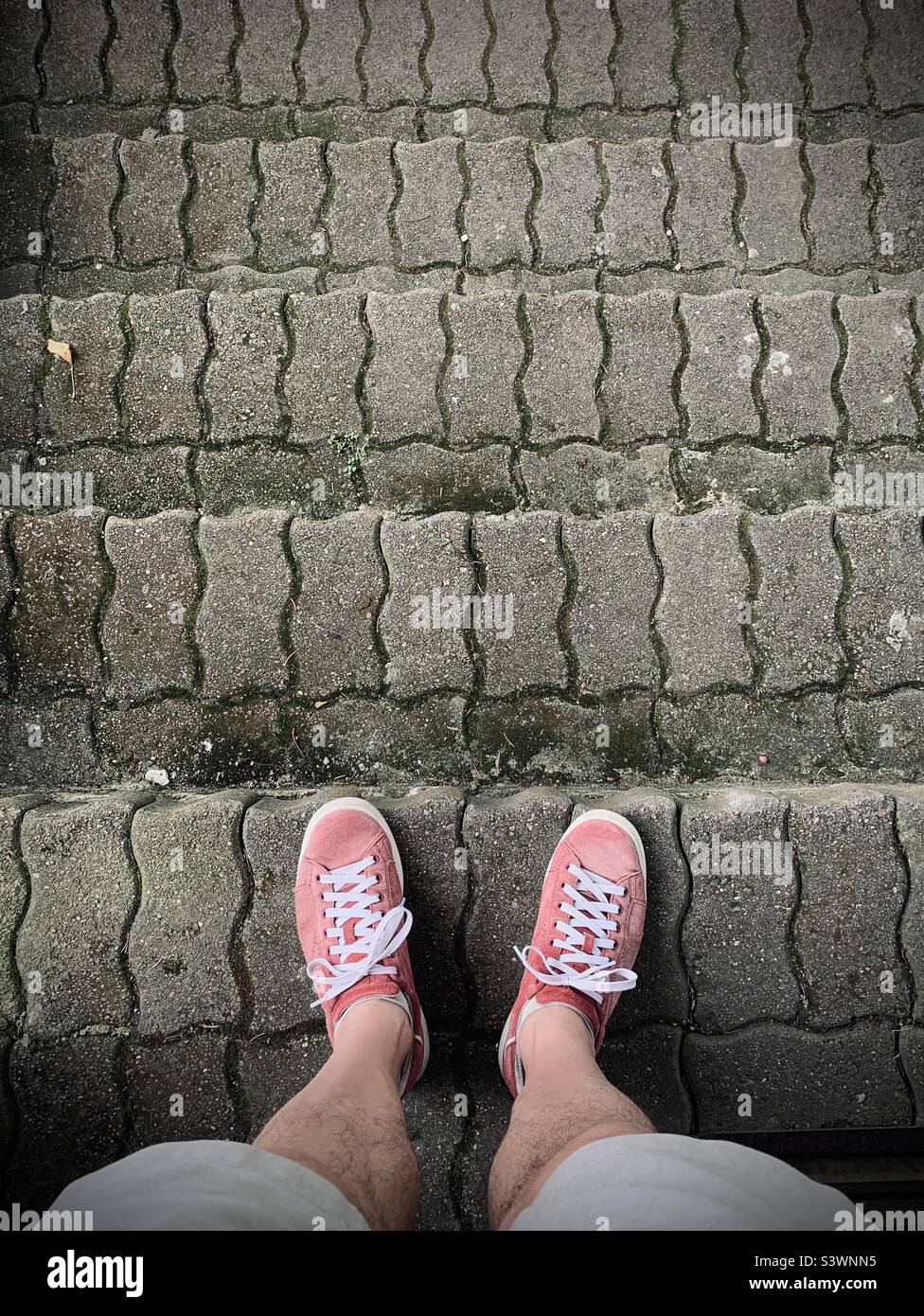 Mens feet with red sneakers from above on grey pavement - Smartphone Captured Stock Image