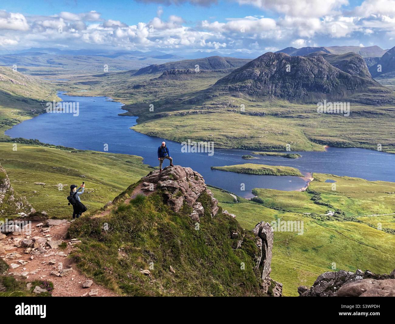 Walkers taking a photograph on the ridge of Stac Pollaidh or Stack Polly, mountain in Inverpolly, with a view of Loch Lurgainn, North West Scotland - Smartphone Captured Stock Image