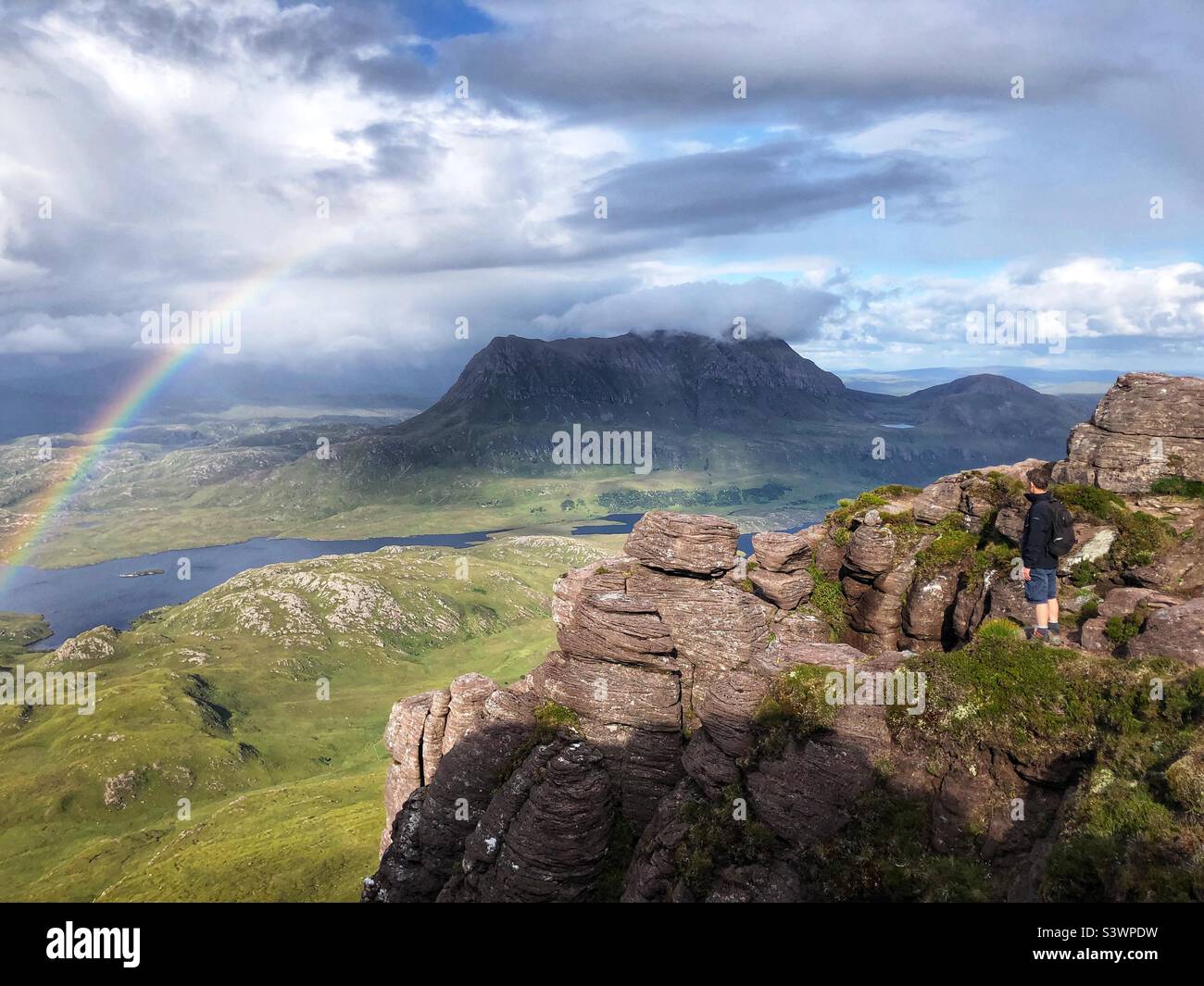 Walker on the ridge of Stac Pollaidh or Stack Polly, mountain in Inverpolly, with a view towards the mountain Cul Mor with a rainbow display, North West Scotland - Smartphone Captured Stock Image
