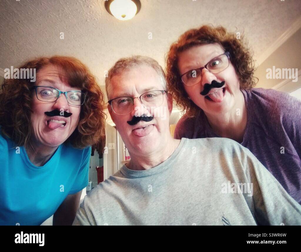 Brother and sisters ham it up wearing false mustaches for the camera. - Smartphone Captured Stock Image