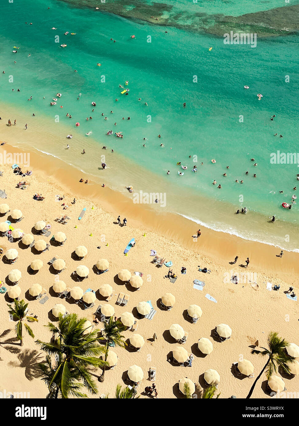 High angle view of beach umbrellas and beach goers on a sandy beach and in the warm waters in Hawaii. - Smartphone Captured Stock Image