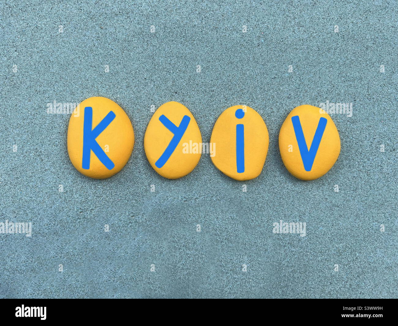 Kyiv, capitol of Ukraine composed with yellow and blue hand painted stone letters over green sand Stock Photo