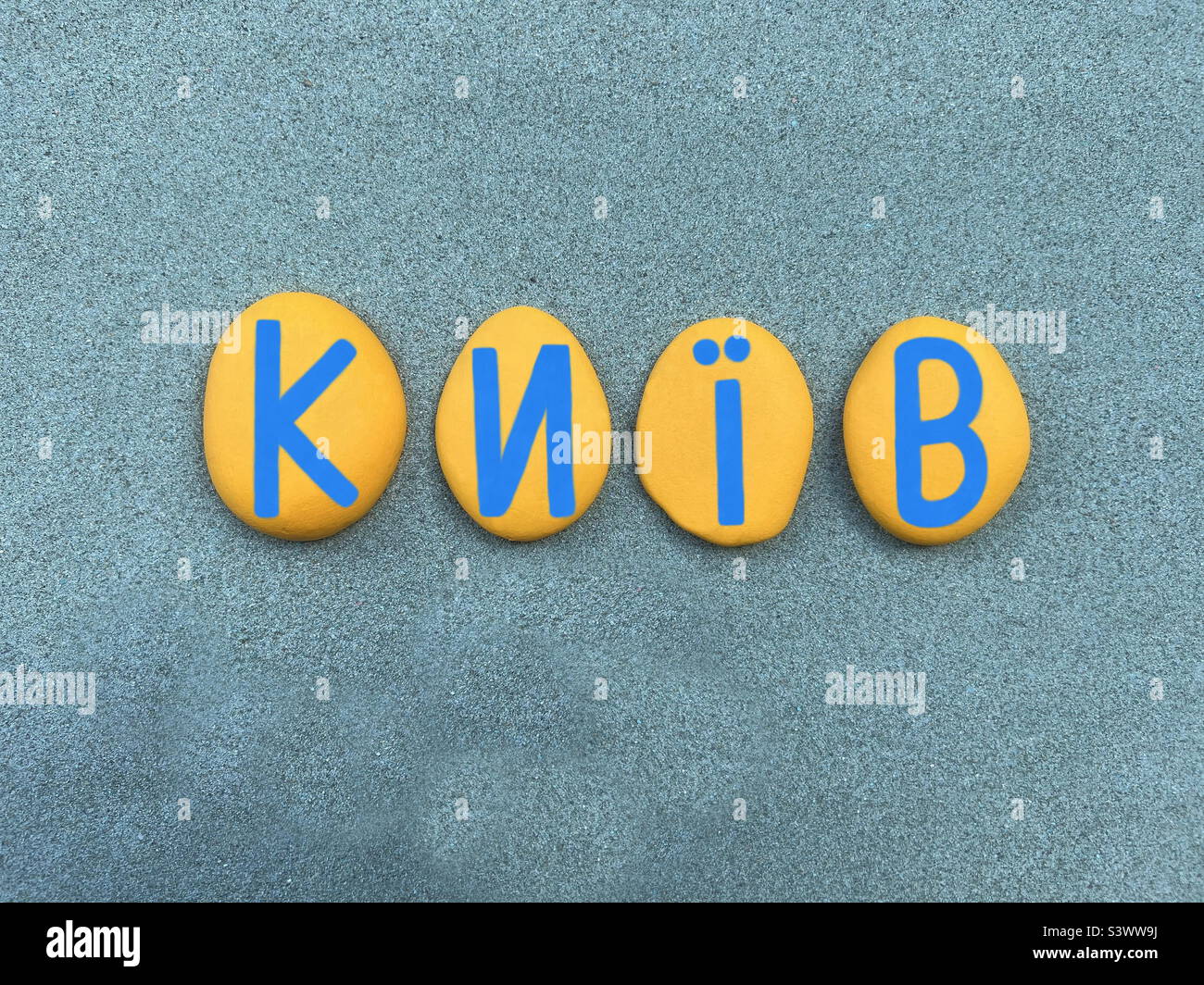 Kiev, capitol of Ukraine composed with yellow and blue hand painted stone Ukrainian letters over green sand Stock Photo