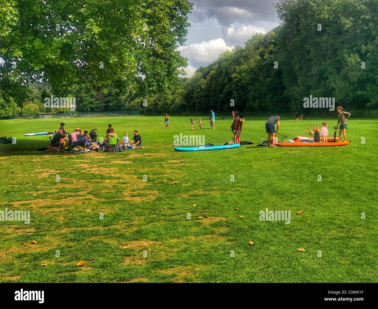 Families picnicking and inflating paddle boards on a Winchester Park, Hampshire United Kingdom. August 2022. - Smartphone Captured Stock Image