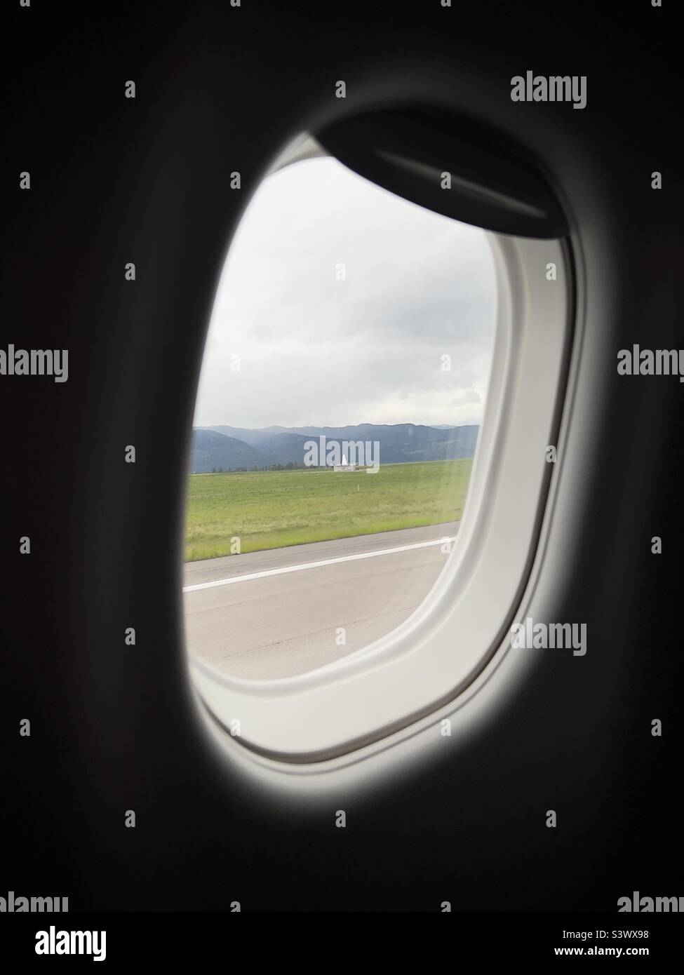 Radar navigation building, now replaced with GPS systems, with mountains behind, seen through passenger jet window while taxiing to runway at Missoula Montana Airport - Smartphone Captured Stock Image