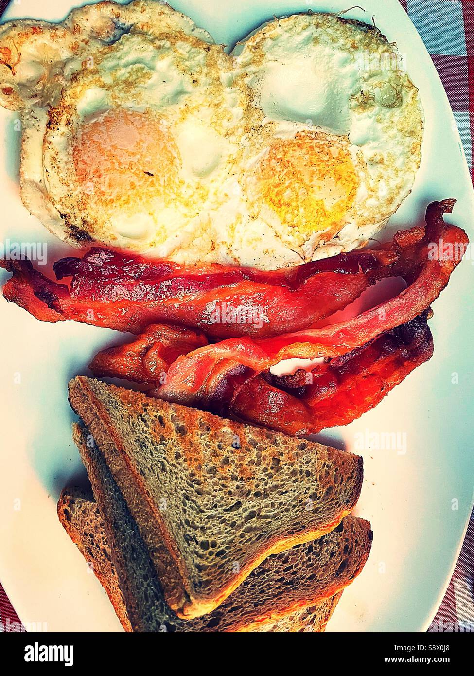Close-up of a hearty breakfast of two eggs over easy, strips of bacon and rye toast, 2022, NYC, USA Stock Photo
