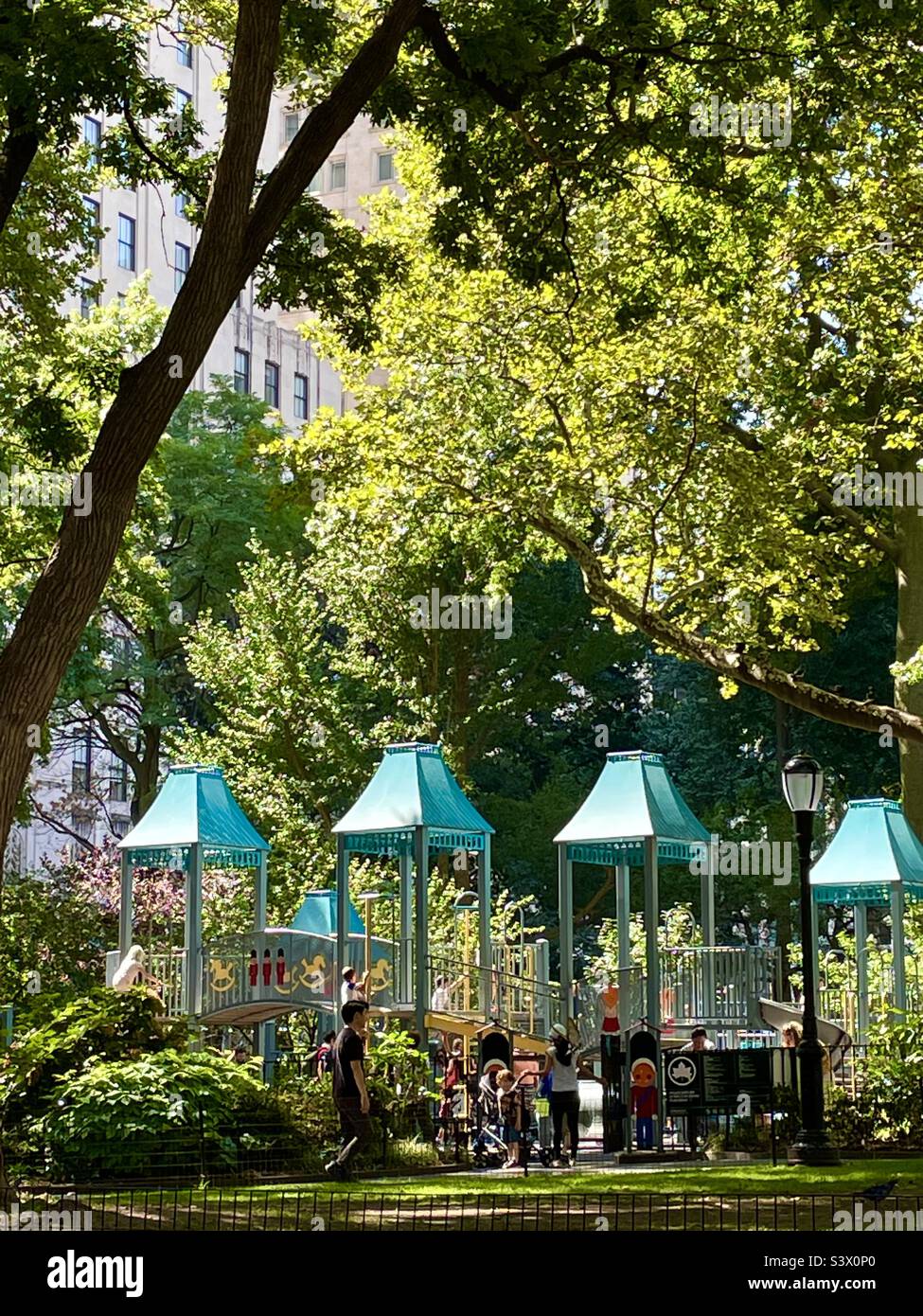 A late summer view of the children’s playground with turquoise blue towers nestled in trees in Madison Square, Park, New York City, USA - Smartphone Captured Stock Image