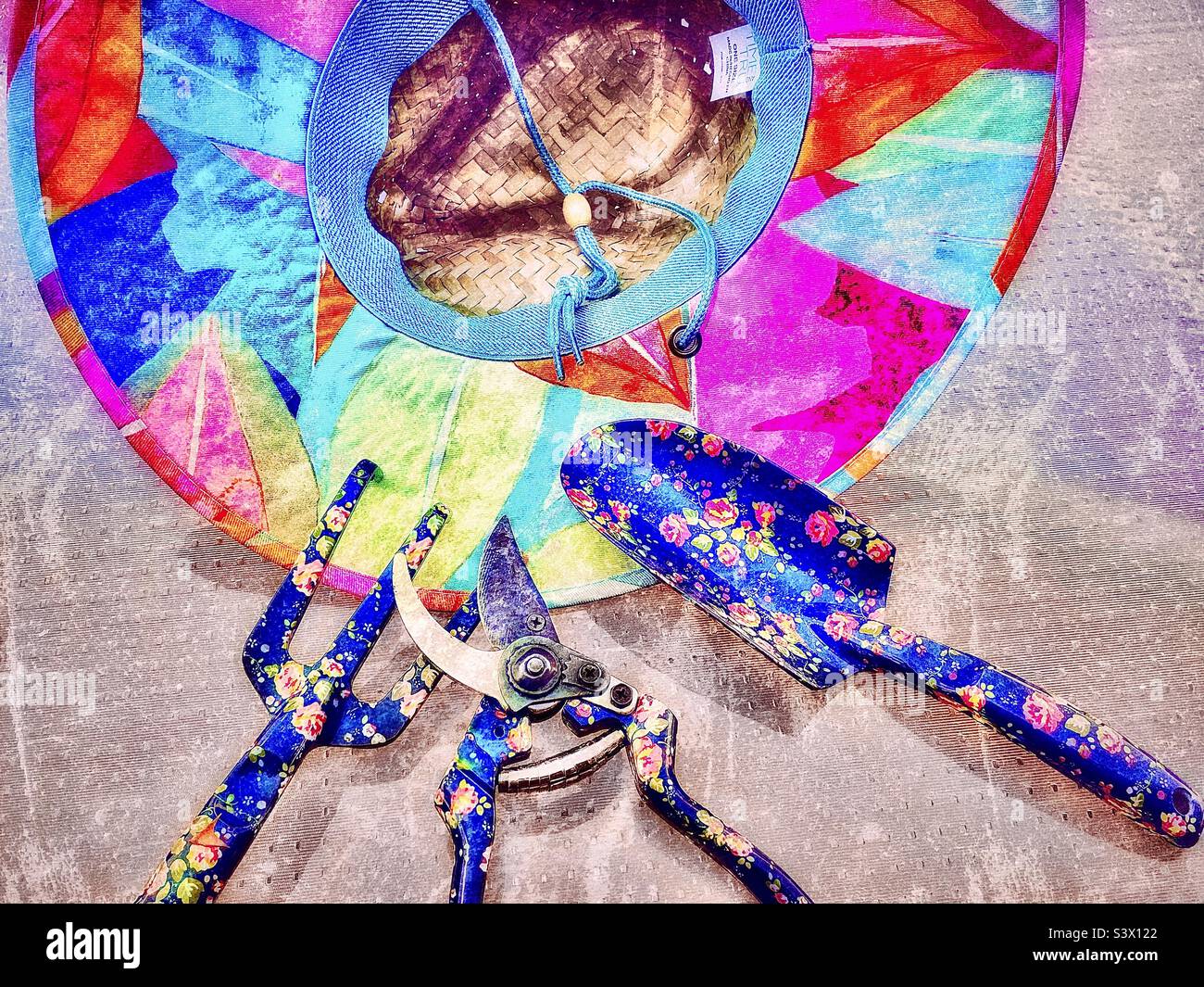 A female gardener’s tools for working out in her yard/garden - a colorful straw hat, and flowery pruning shears, spade and claw. Grunge effect digitally added to this outdoor still life. - Smartphone Captured Stock Image