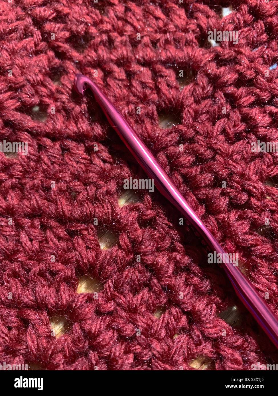 Rust-coloured crocheted blanket in chevron pattern with red aluminum crochet hook Stock Photo