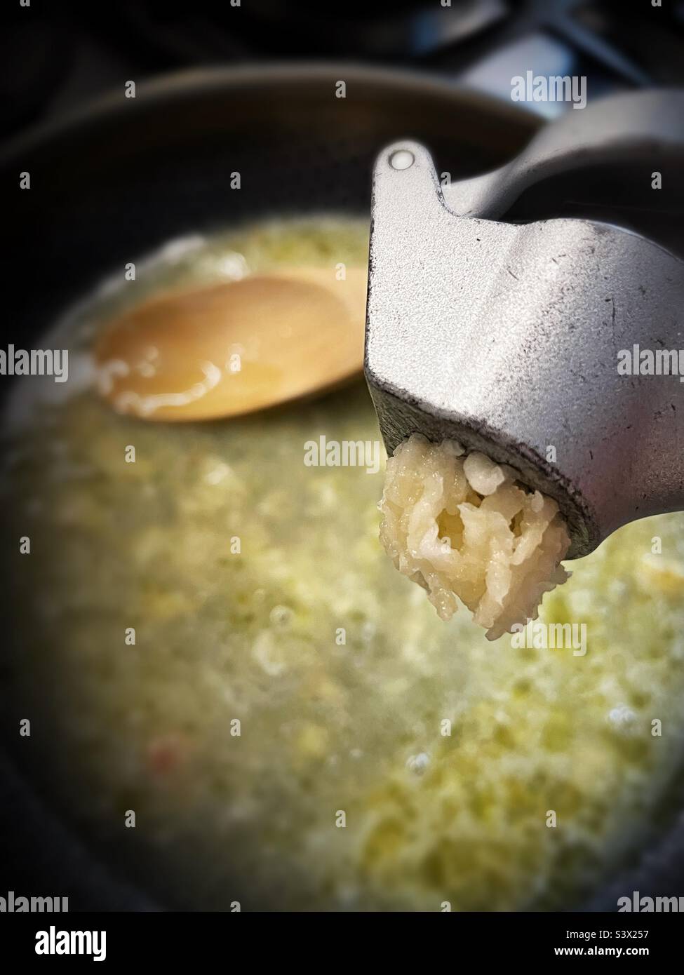 Garlic press adding fresh garlic to a simmering sauce pan, 2022, USA Stock Photo