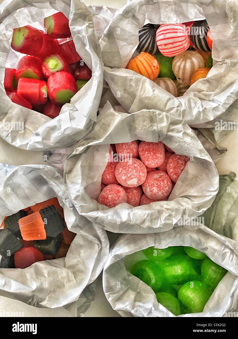 Traditional old fashioned sweets in paper bags rhubarb rock, soor plooms, midget gems, cinnamon balls, humbugs striped balls Stock Photo